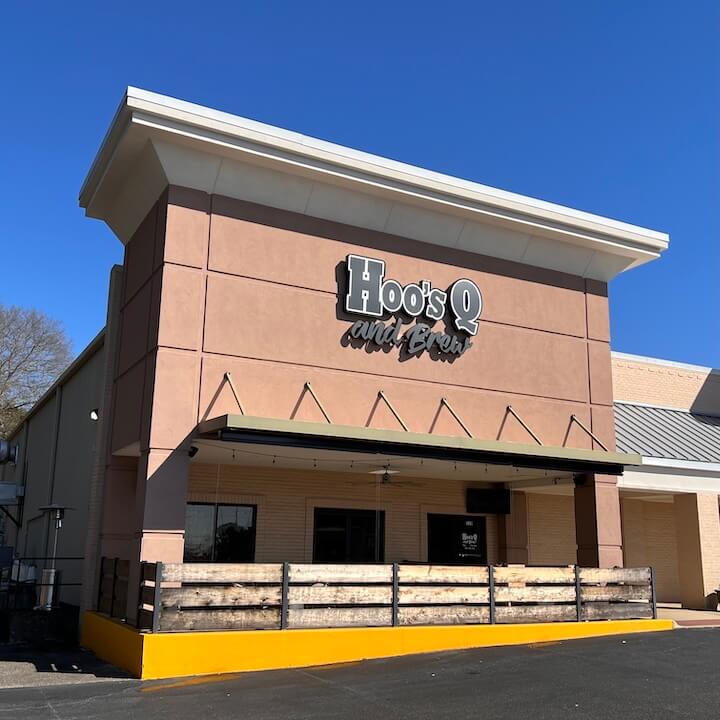 A brick building featuring outdoor seating and a sign reading 'HoosQ' in Tuscaloosa, Alabama.