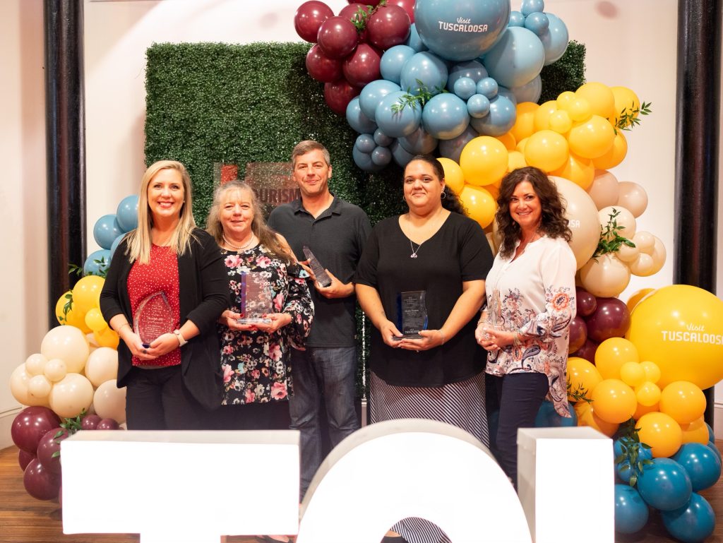 Group photo taken in front of red, blue and gold balloon arch. Facing the camera from left to right are Heather Dill, Sandra Fincher, Craig Williams, Heide Patton and Chereé Slaten