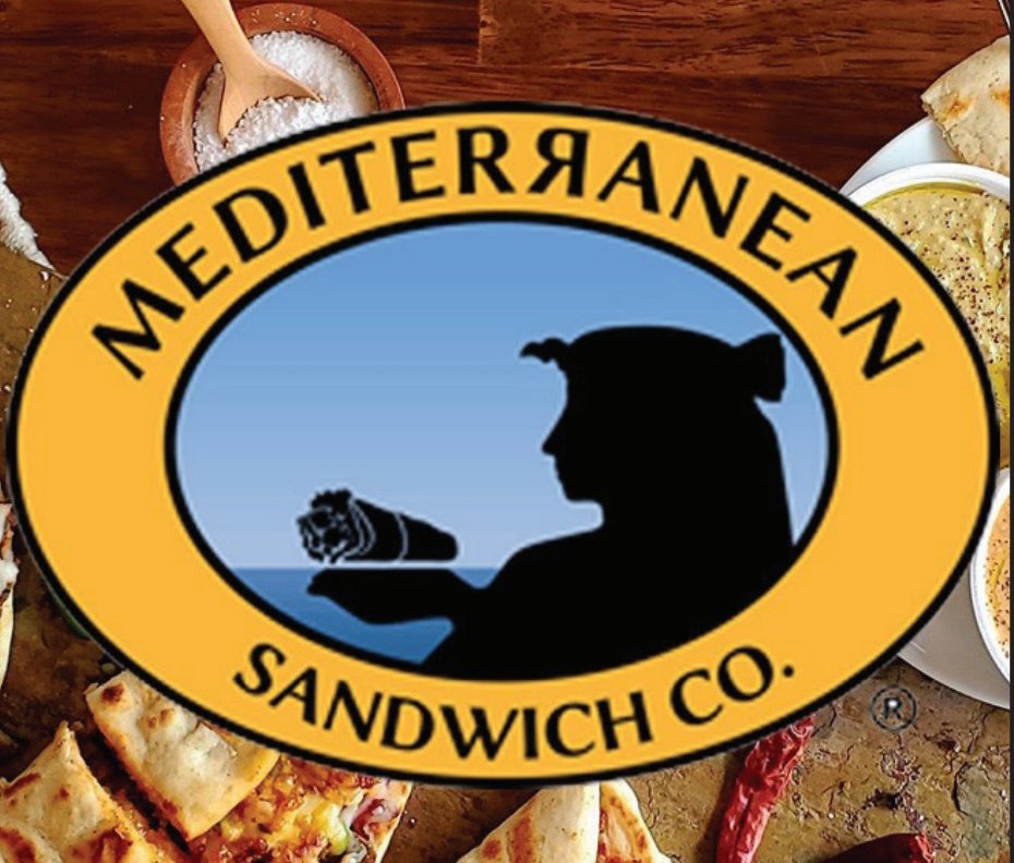 Mediterranean-style sandwiches and dishes displayed on a rustic wooden table in Tuscaloosa, Alabama.