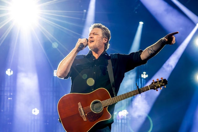 A person with an acoustic guitar holding a microphone and singing