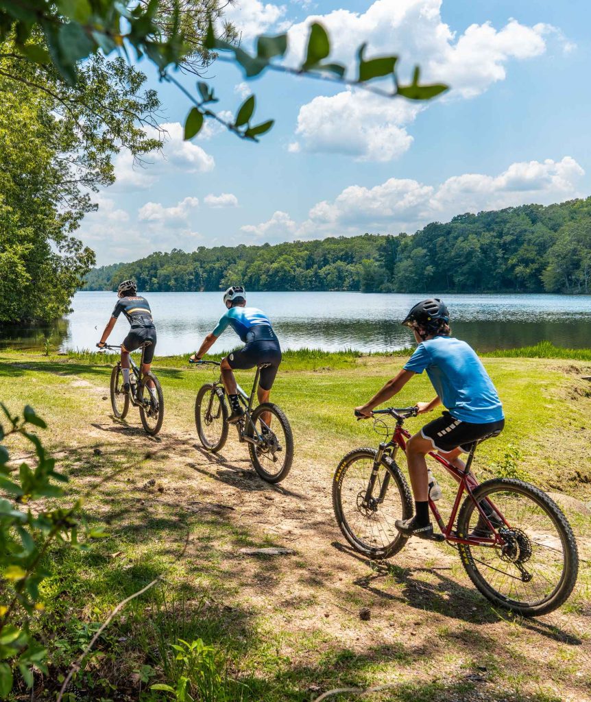 Three cyclists riding an offroad trail with a view of Lake Lurleen in the background.