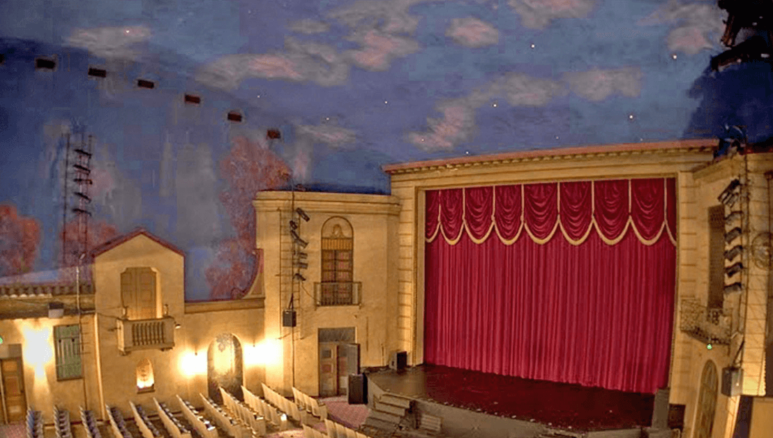 This new image is a beautiful, historic interior. For SEO and a strong description, here is the alt text: The Historic Bama Theatre in Tuscaloosa, AL, showing the vintage interior with a large red curtain stage, ornate balconies, and seating in the auditorium.