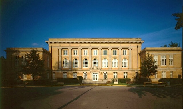 A majestic, classical building with large windows and a grand entrance, called Smith Hall, set against a clear blue sky in Tuscaloosa, Alabama on The University of Alabama campus.