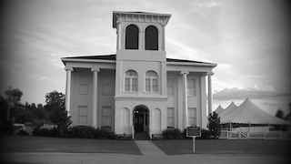 A grand, historic building with a distinctive tower, called The Historic Drish House, set against a cloudy sky in Tuscaloosa, Alabama.