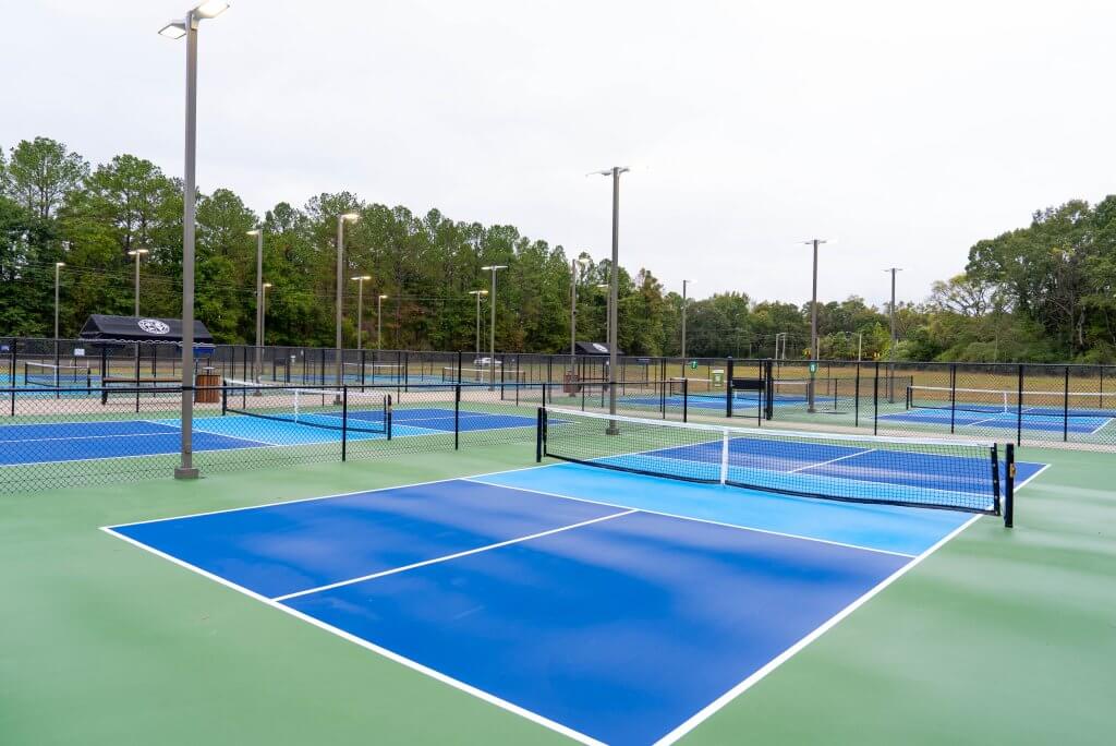 A well-maintained outdoor tennis complex with multiple courts, surrounded by trees and illuminated by tall light poles