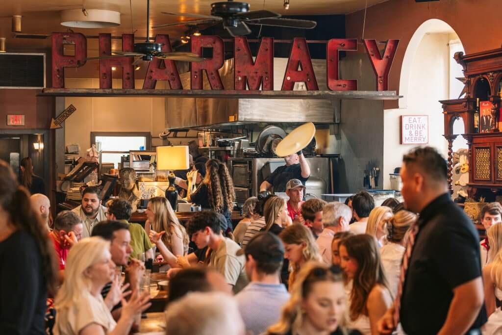 A bustling restaurant filled with patrons enjoying their meals and drinks under a large, illuminated 'PHARMACY' sign
