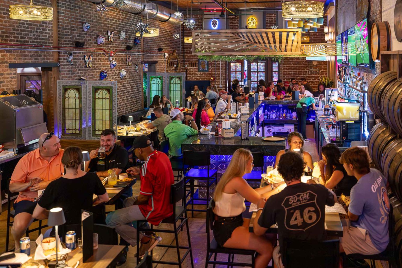 A lively bar scene with patrons enjoying drinks and meals at tables and the bar, surrounded by eclectic decor and exposed brick walls