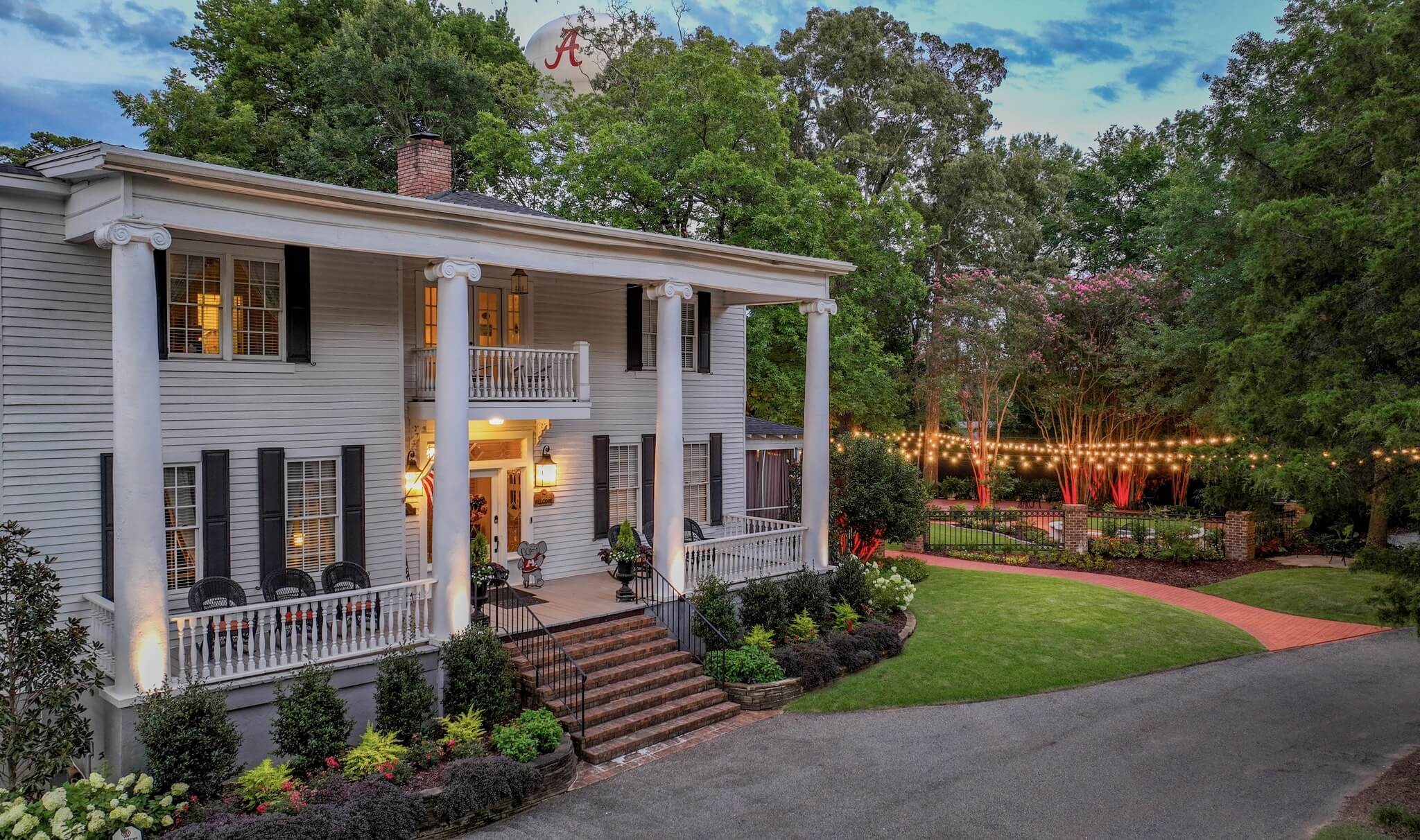 A charming white Victorian house with a porch, surrounded by lush greenery and twinkling lights in Tuscaloosa, Alabama called Bama Bed & Breakfast