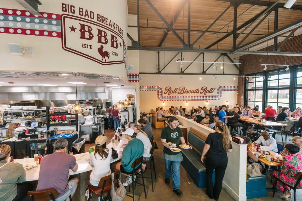 A bustling restaurant called Big Bad Breakfast near the University of Alabama campus with a retro vibe, featuring a large sign and a lively atmosphere in Tuscaloosa, Alabama.