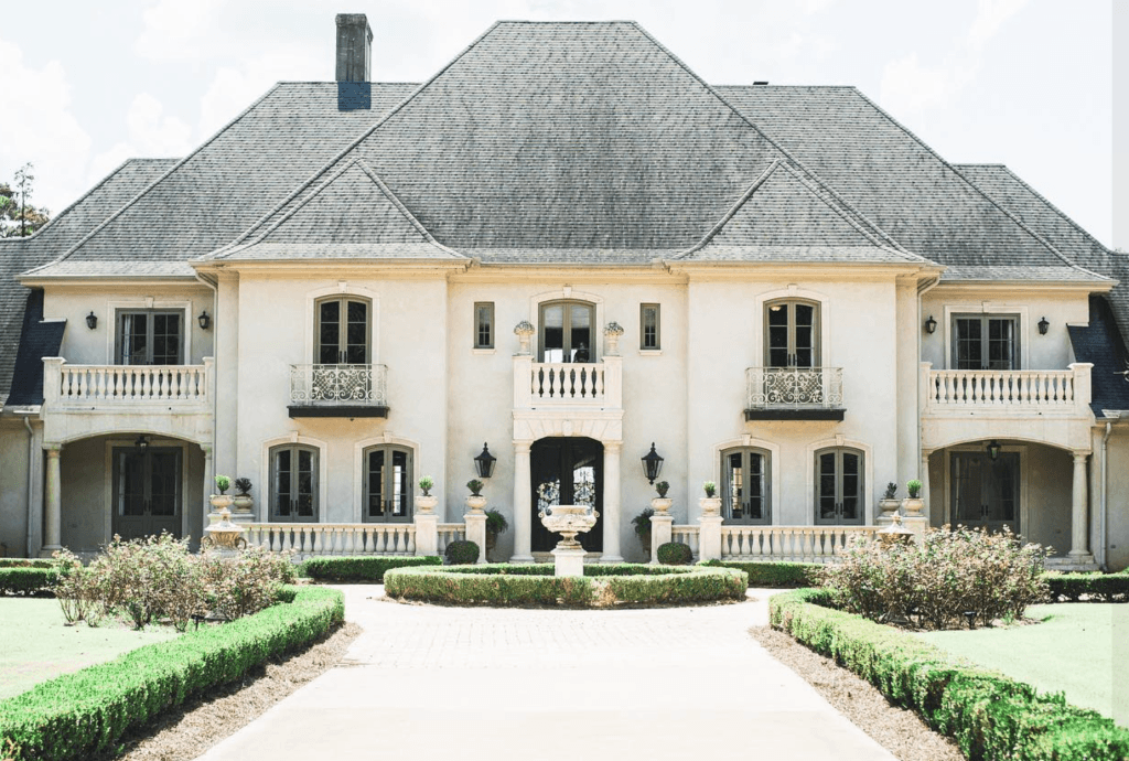 An opulent, large mansion with a distinctive roof, elegant balconies, and lush landscaping