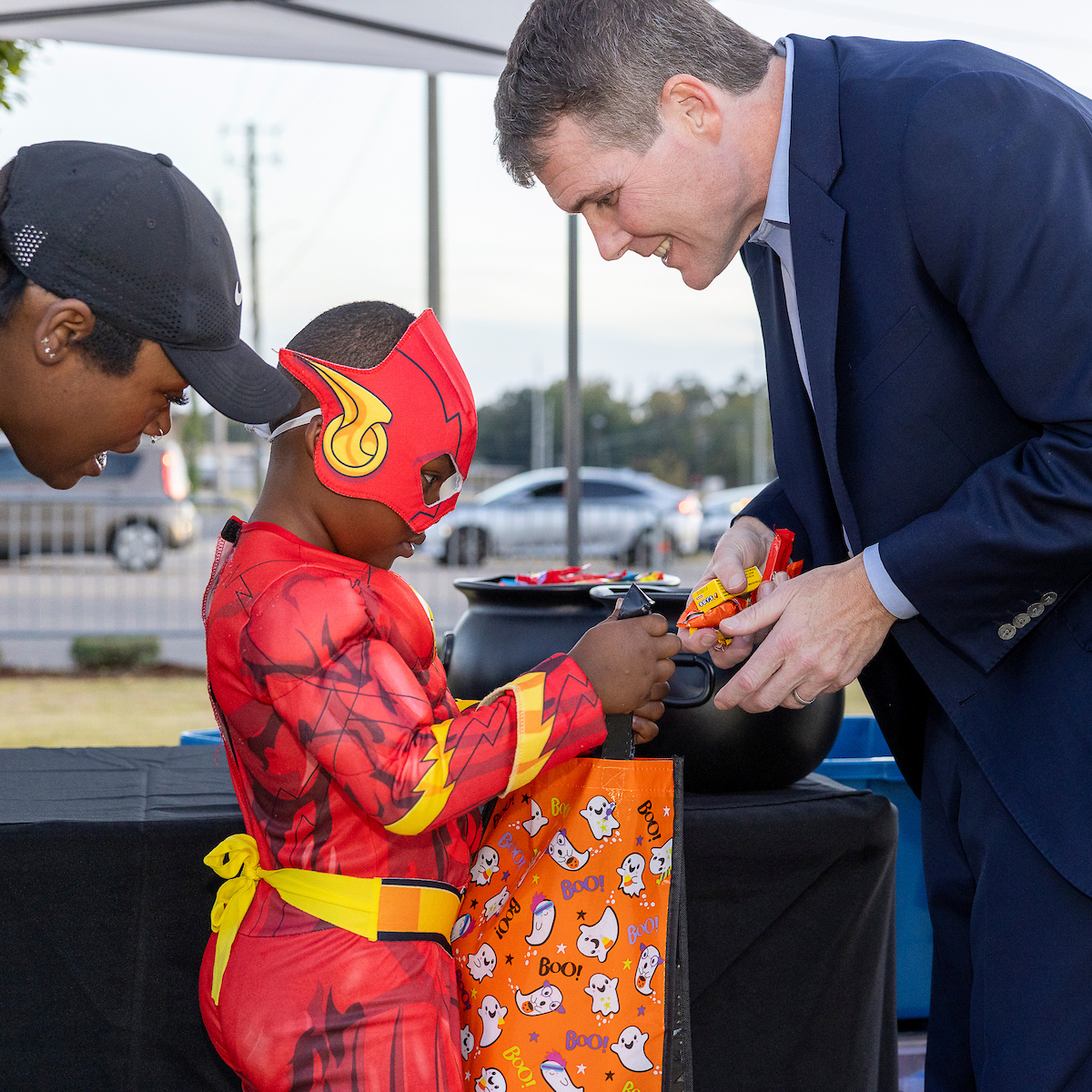 A child in a red superhero costume receives candy from a man in a suit