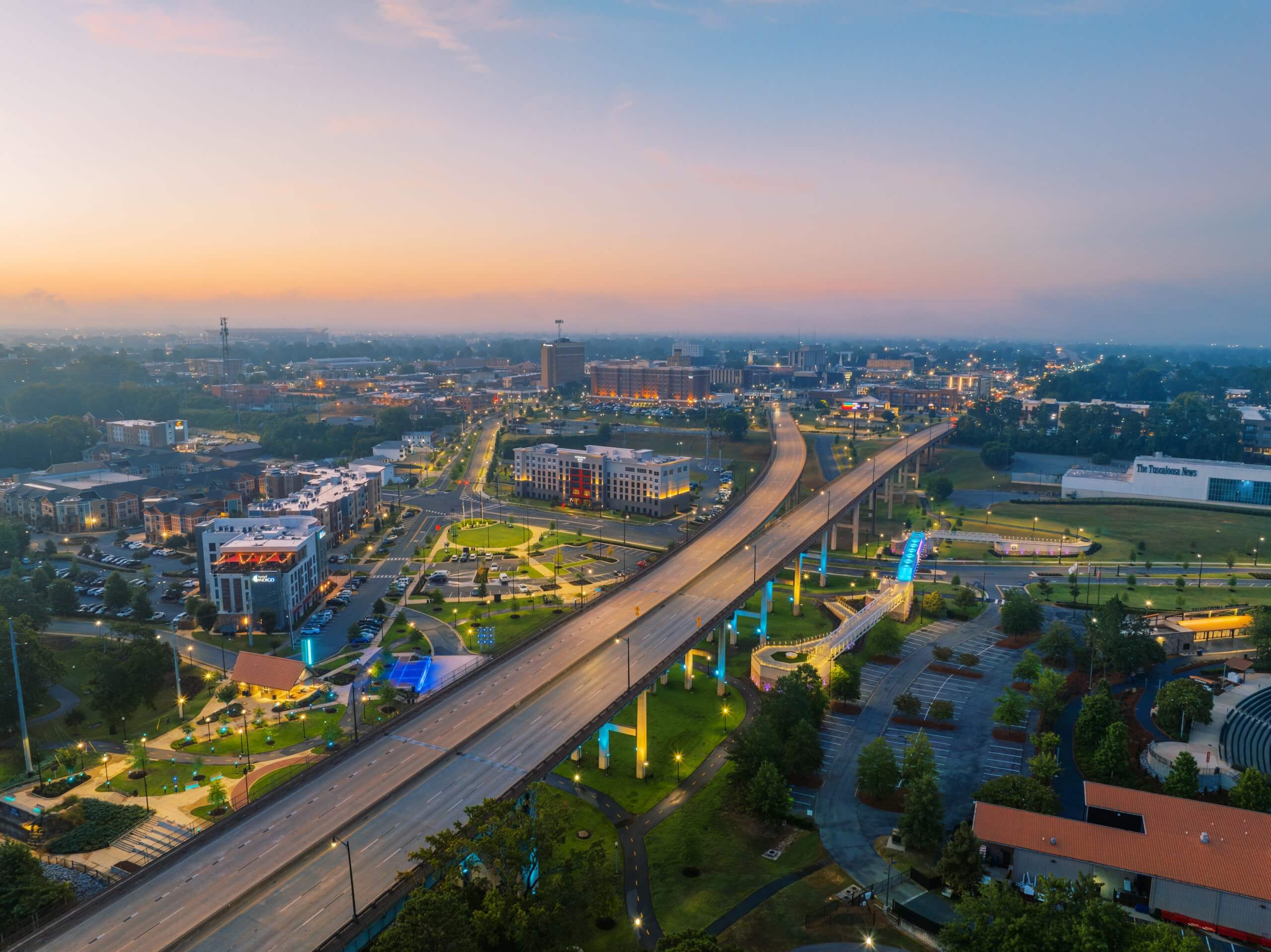 A cityscape at dawn with a highway, bridges, and illuminated buildings in Downtown Tuscaloosa, Alabama.