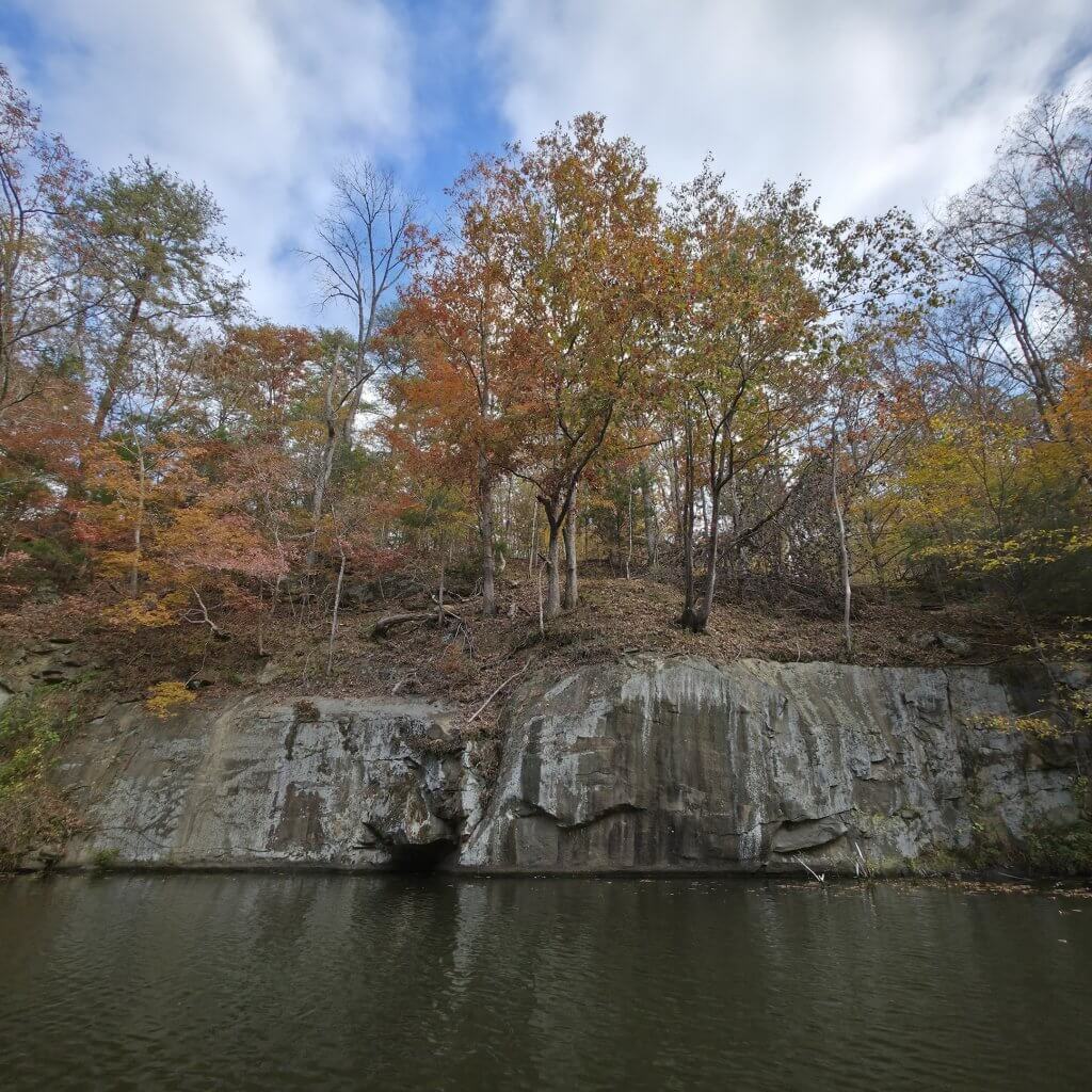 A serene autumn scene with a calm river reflecting the vibrant colors of the changing leaves on the forested hillside in Tuscaloosa, Alabama.