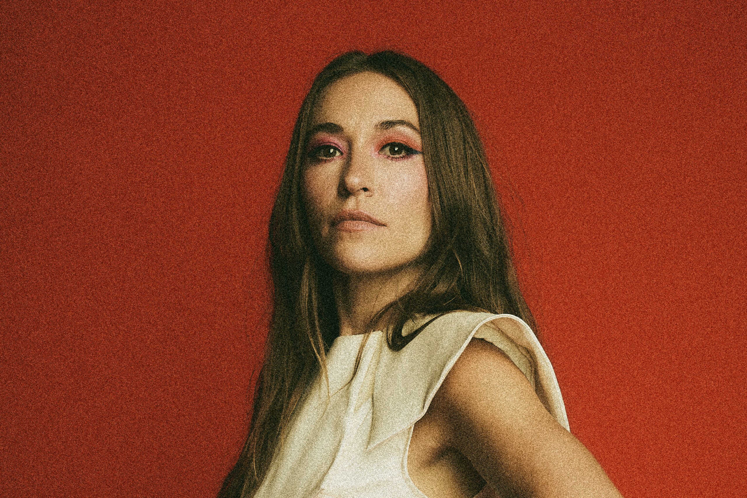 A woman with bold makeup stands confidently against a vibrant red background in Tuscaloosa, Alabama.