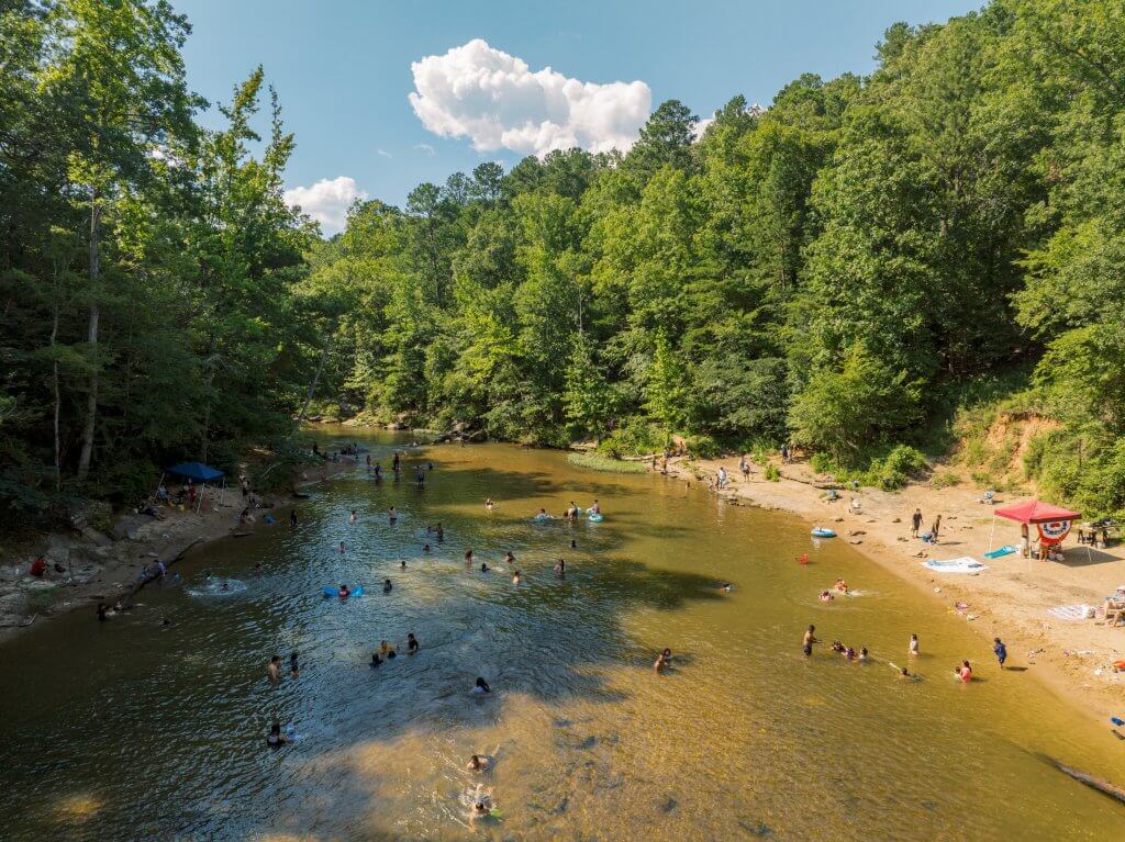 A bustling river scene at Hurricane Creek with people swimming and relaxing on a sunny day in Tuscaloosa, Alabama.