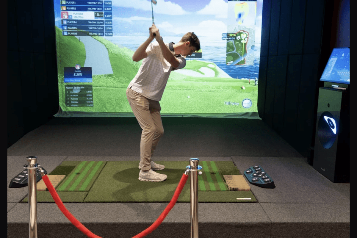A young golfer practicing his swing in Ember & Ice, a virtual golf simulator in Tuscaloosa, Alabama.