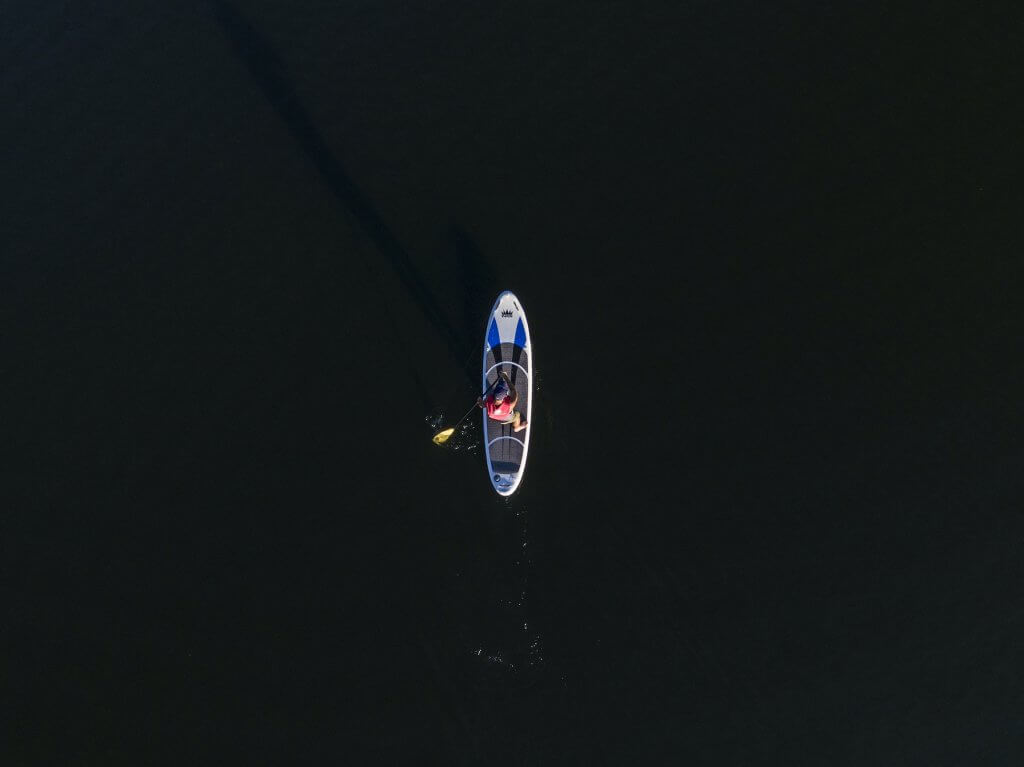 A lone paddler glides silently on a sleek stand-up paddleboard across the dark, calm waters of a lake at night in Tuscaloosa, Alabama on Lake Tuscaloosa.