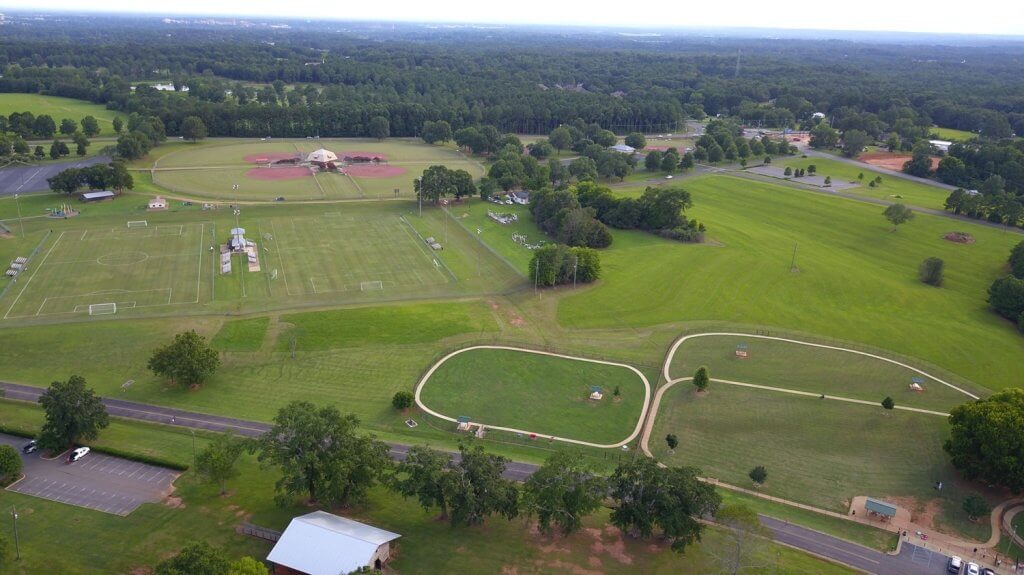 A sprawling park with sports fields, walking paths, and picnic areas surrounded by lush greenery in Tuscaloosa, Alabama.