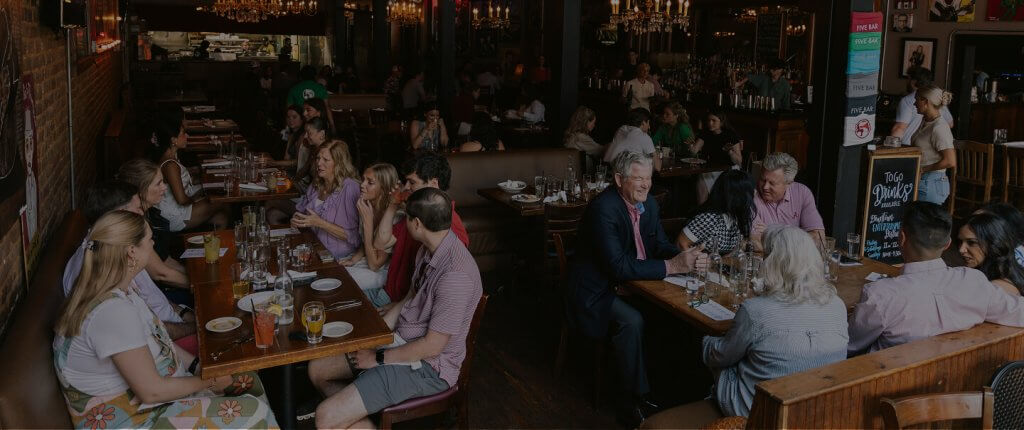 A lively restaurant filled with patrons enjoying meals and drinks at wooden tables in Tuscaloosa, Alabama.