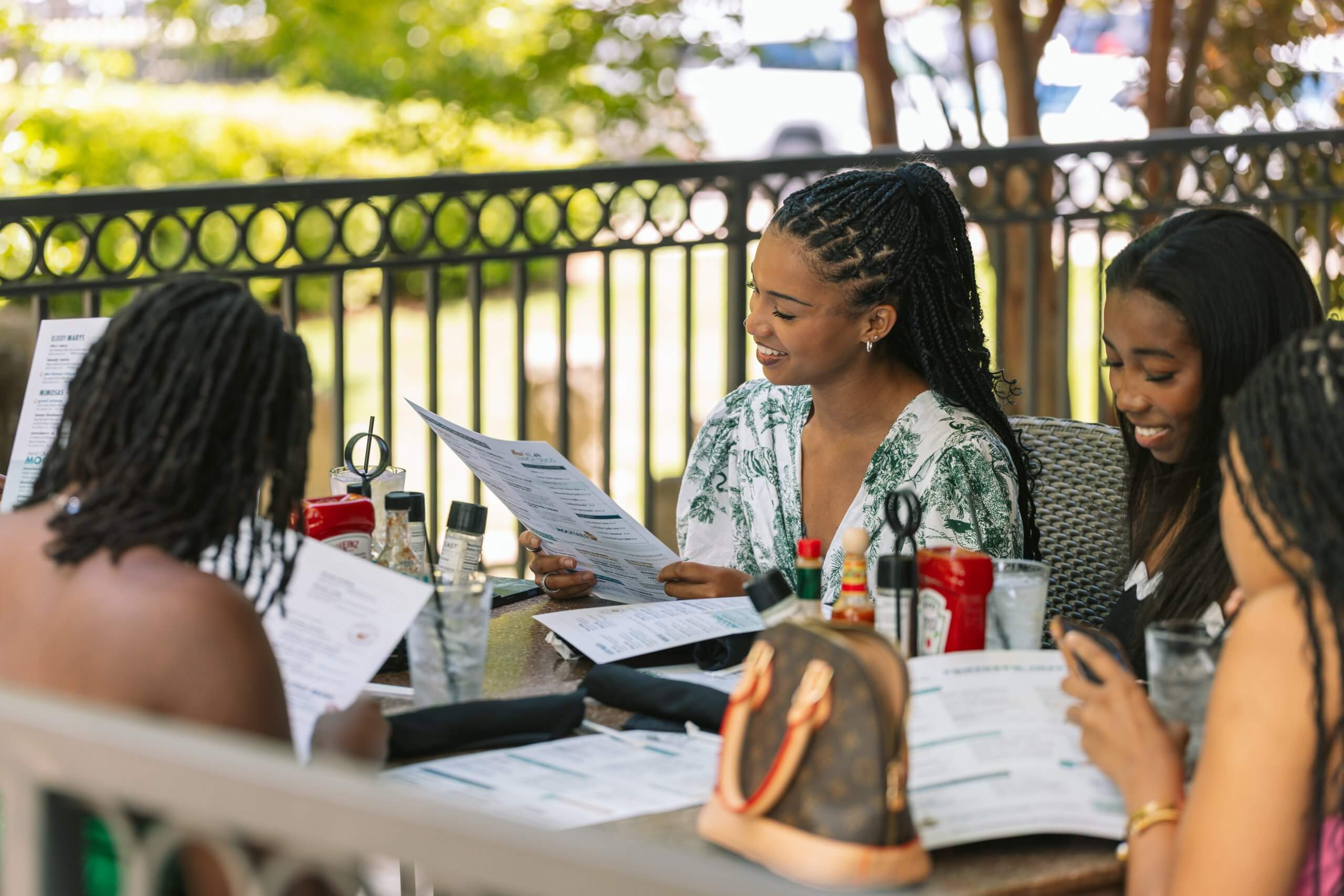 Four women are enjoying a meal together at an outdoor restaurant, laughing and reading menus in Tuscaloosa, Alabama.