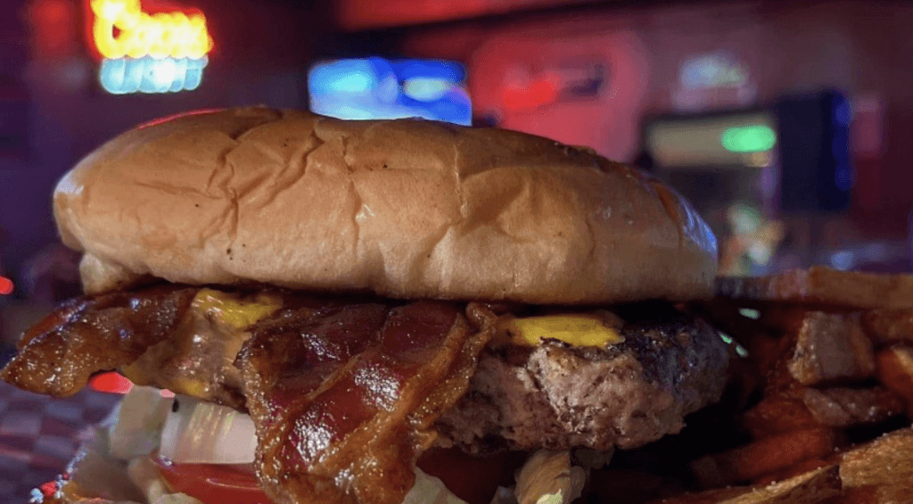 A mouthwatering bacon cheeseburger with crispy fries in a dimly lit diner setting in Tuscaloosa, Alabama.