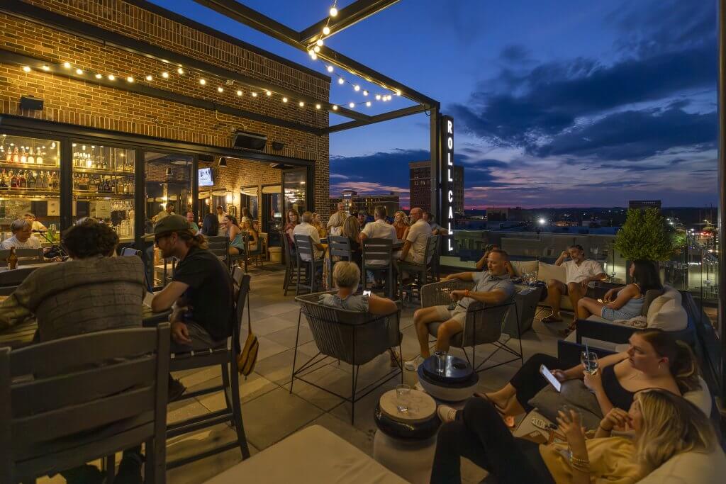 Patrons enjoy drinks and conversation at an outdoor rooftop bar as the sun sets over the city skyline in Tuscaloosa, Alabama.