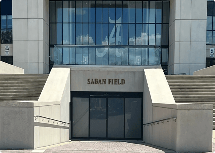 A modern stadium entrance with steps leading up to glass doors, labeled 'Saban Field' with an 'A' logo in Tuscaloosa, Alabama.