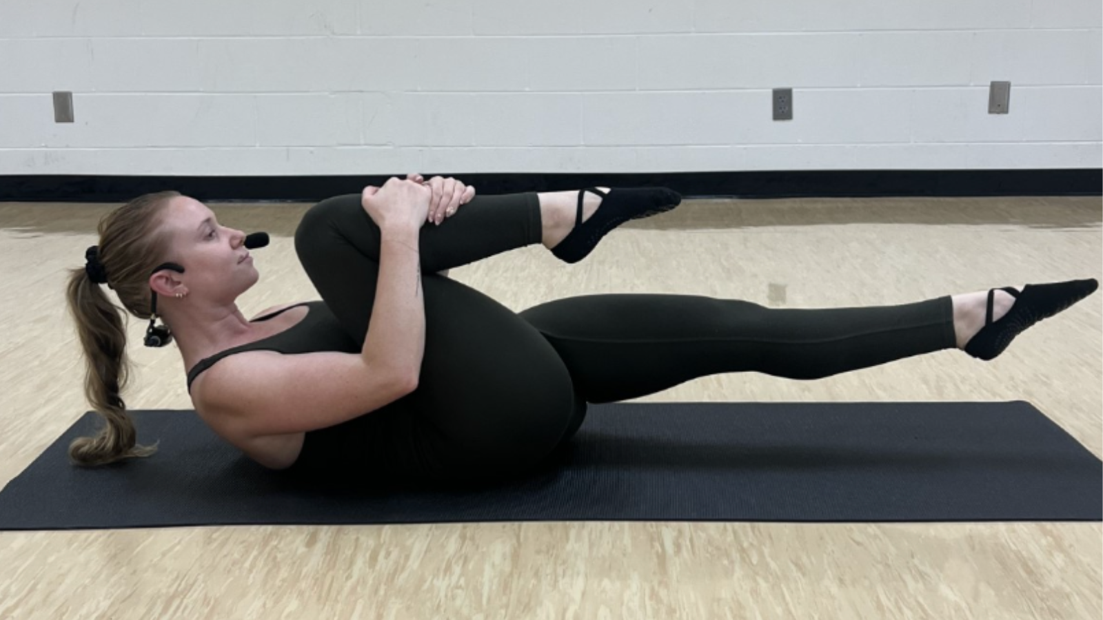 A woman in a black leotard and leg warmers performs a yoga pose on a black mat in a dance studio in Tuscaloosa, Alabama.