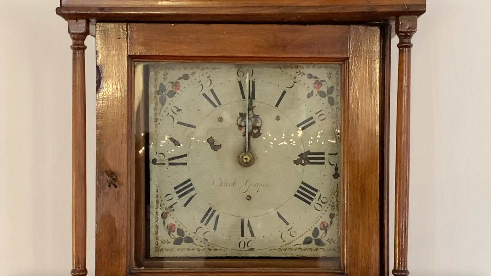 An antique wooden grandfather clock with a worn face and floral decorations in Tuscaloosa, Alabama.