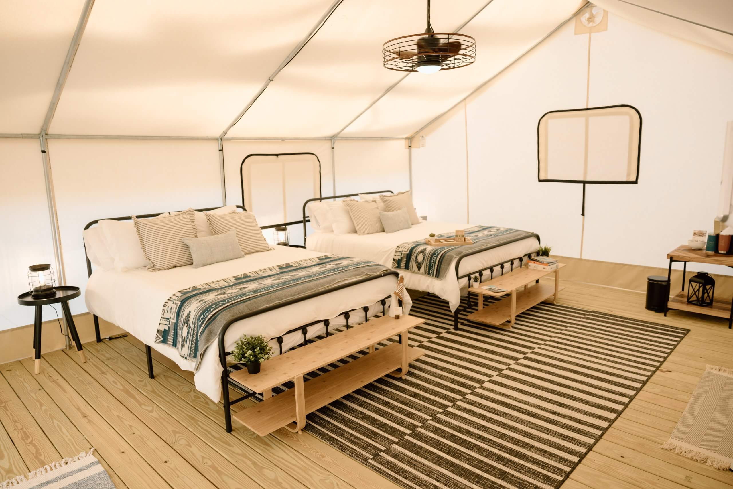 A cozy glamping tent with two beds, each adorned with striped pillows and a blue and white blanket, set on a wooden floor with a striped rug in Tuscaloosa, Alabama.