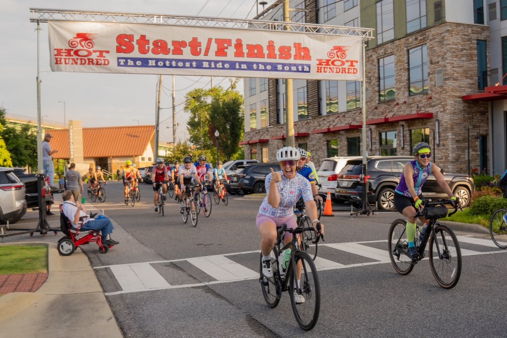 Cyclists cross the finish line of the Hot Hundred bike race, celebrating their achievement in Tuscaloosa, Alabama.