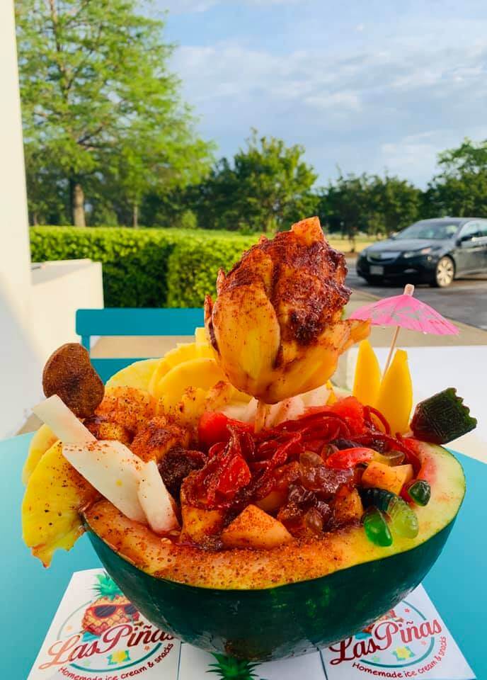 A vibrant fruit bowl topped with a fiery dragon fruit centerpiece, served in a hollowed-out watermelon and garnished with colorful candies and an umbrella in Tuscaloosa, Alabama.