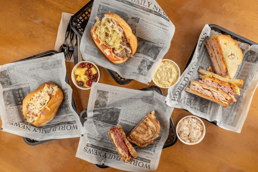 Assorted sandwiches and sides served on newspaper-lined trays in Tuscaloosa, Alabama.