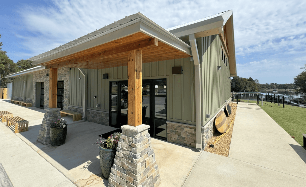 A charming lakeside building with a wooden deck, stone pillars, and green siding, surrounded by lush greenery and a serene lake view in Tuscaloosa, Alabama.