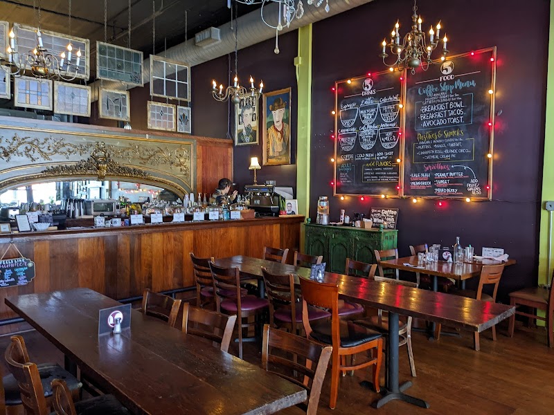 A cozy, vintage-style coffee shop with wooden tables, chairs, and a long bar featuring a chalkboard menu and decorative chandeliers in Tuscaloosa, Alabama.