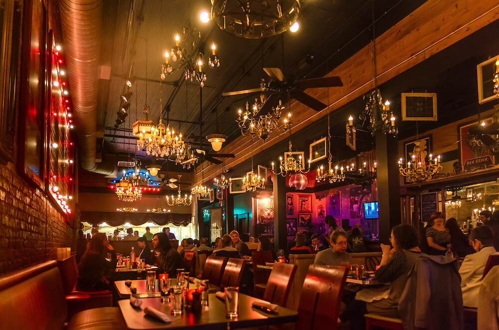 A dimly lit, cozy restaurant with chandeliers and brick walls, filled with patrons enjoying their meals in Tuscaloosa, Alabama.