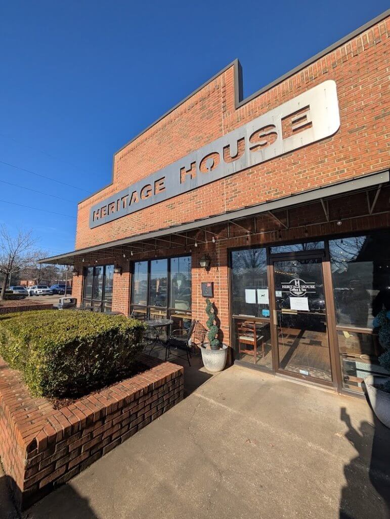 A brick building with a sign reading 'Heritage House' above its entrance, featuring large windows and outdoor seating in Tuscaloosa, Alabama.