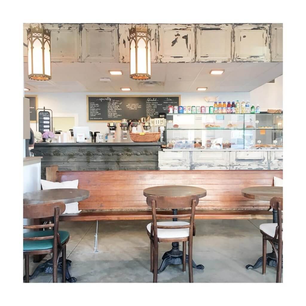 A cozy café interior with wooden benches, round tables, and a rustic counter displaying baked goods and beverages in Tuscaloosa, Alabama.