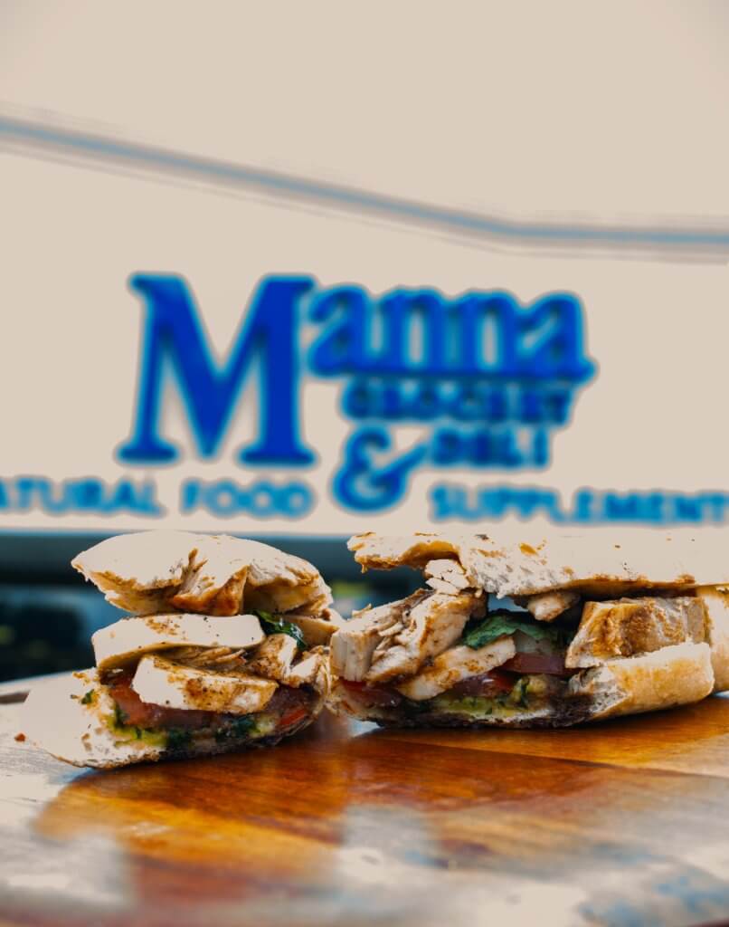 A mouthwatering chicken sandwich with fresh greens and tomatoes, cut in half and presented on a rustic wooden board in Tuscaloosa, Alabama.