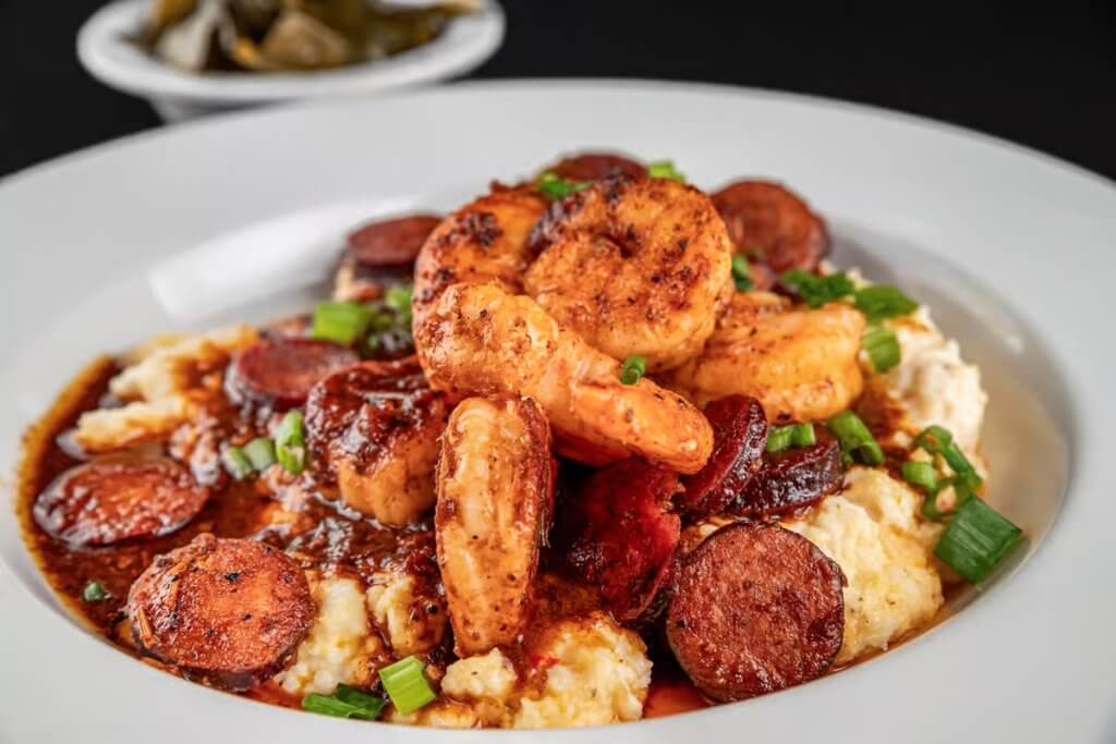 A hearty bowl of shrimp and sausage gumbo served over creamy grits, garnished with green onions in Tuscaloosa, Alabama.