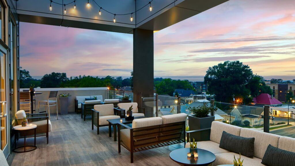 A rooftop patio at dusk with comfortable seating, string lights, and a stunning cityscape view in Tuscaloosa, Alabama.