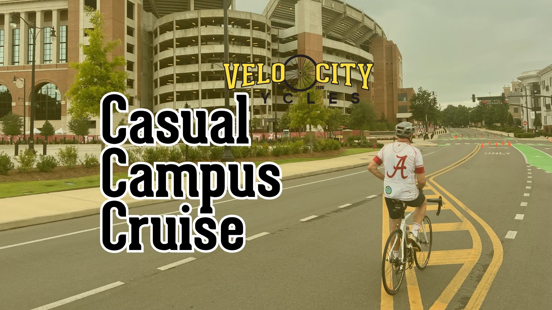 A cyclist wearing an Alabama jersey rides on a road near a large stadium in Tuscaloosa, Alabama.