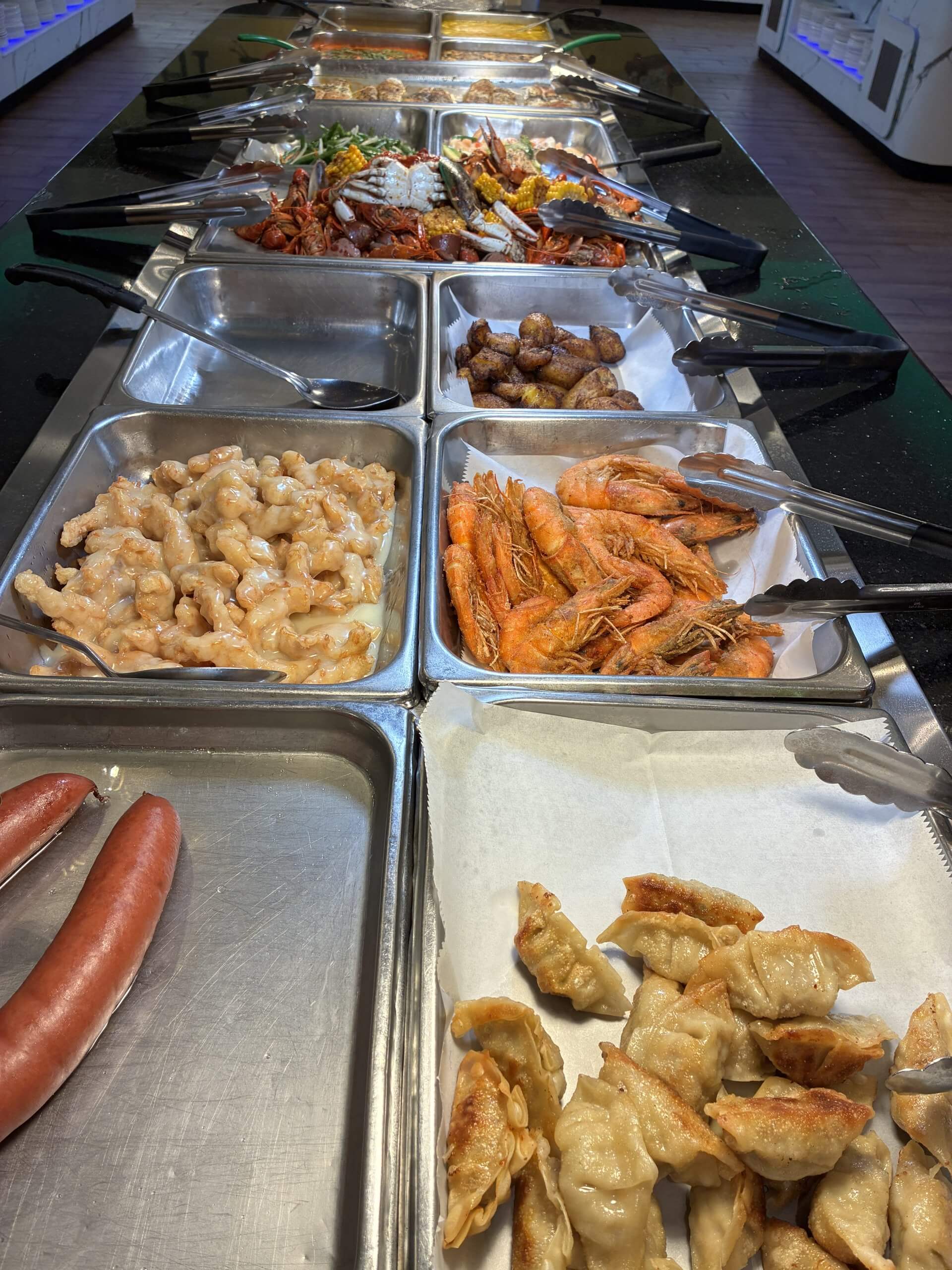 A buffet line featuring various seafood dishes, dumplings, and sausages in metal trays in Tuscaloosa, Alabama.