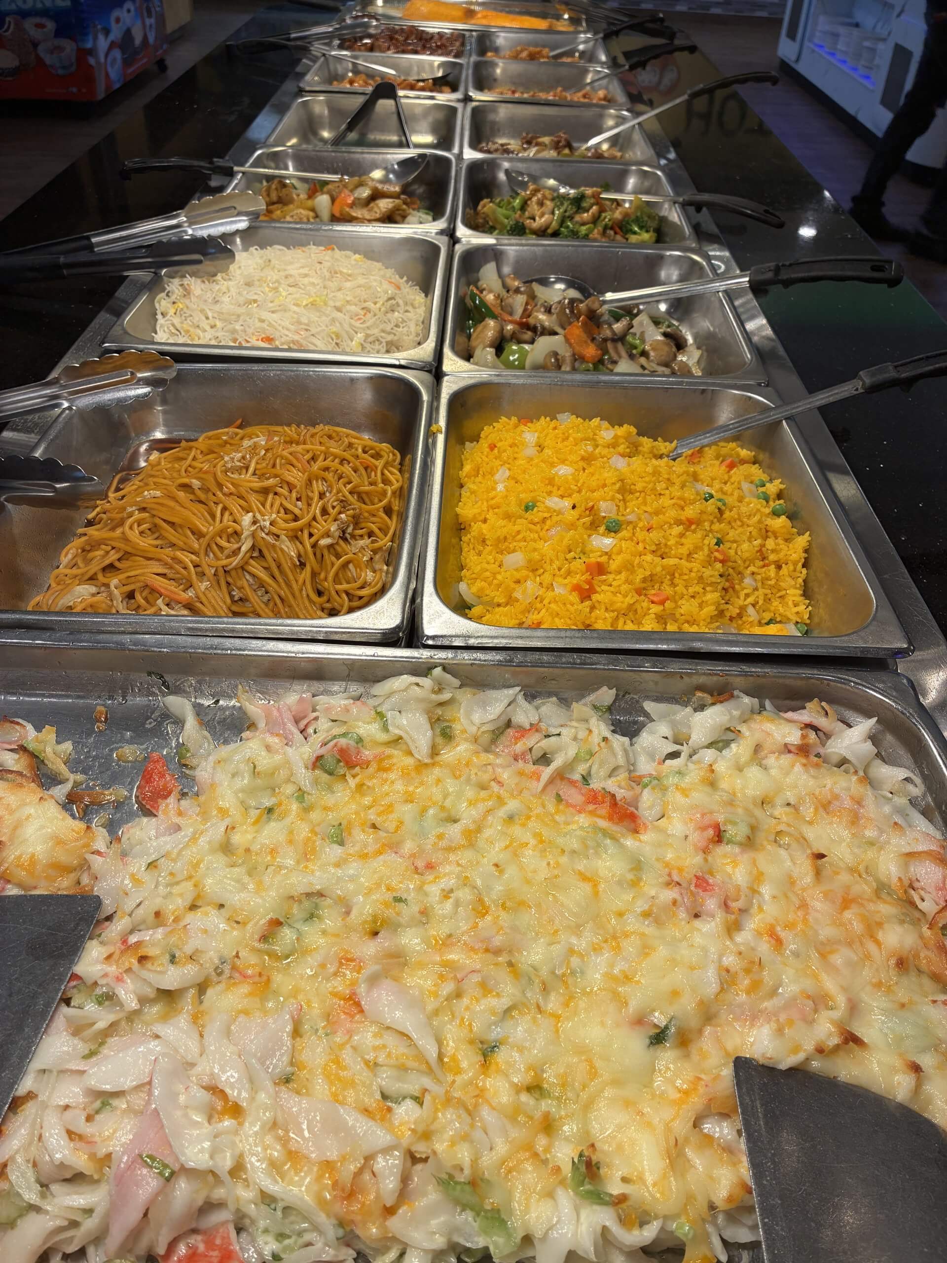 A buffet line featuring various Asian-style dishes in metal serving trays in Tuscaloosa, Alabama.