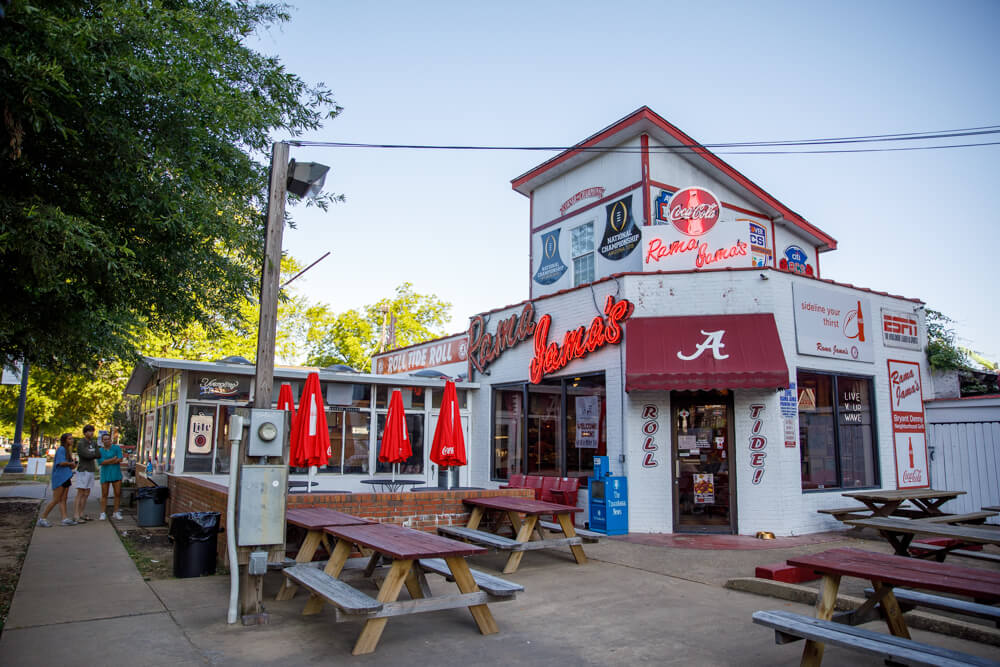 The exterior of Rama Jama's restaurant, an Alabama football tradition, featuring Crimson Tide memorabilia and outdoor seating for in Tuscaloosa, Alabama.