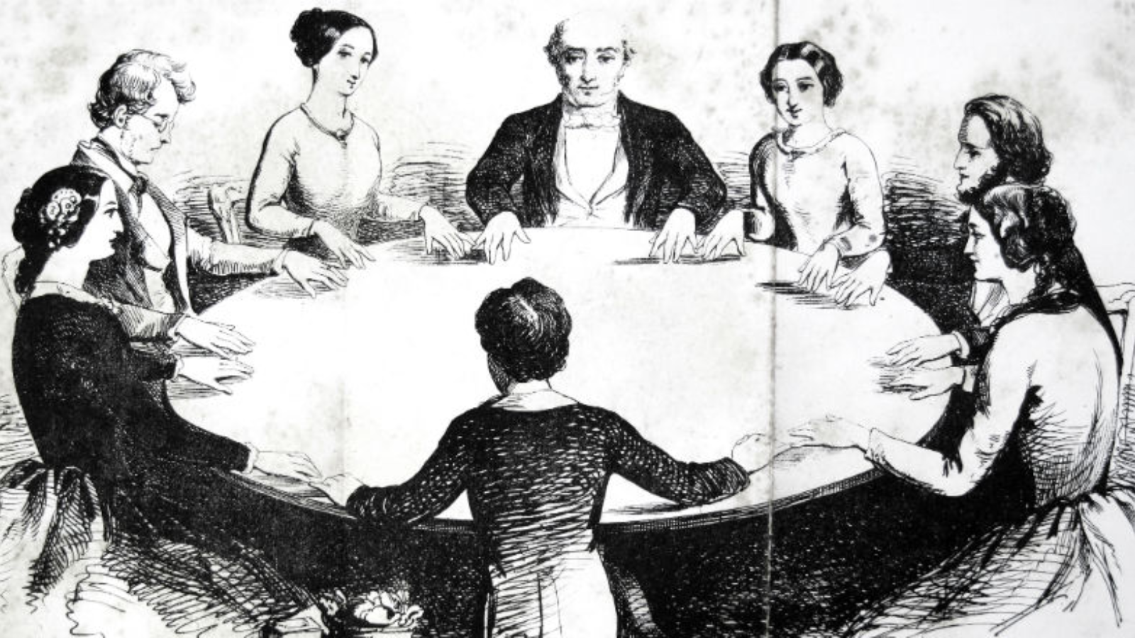 A group of people sitting around a round table participating in a seance in Tuscaloosa, Alabama.