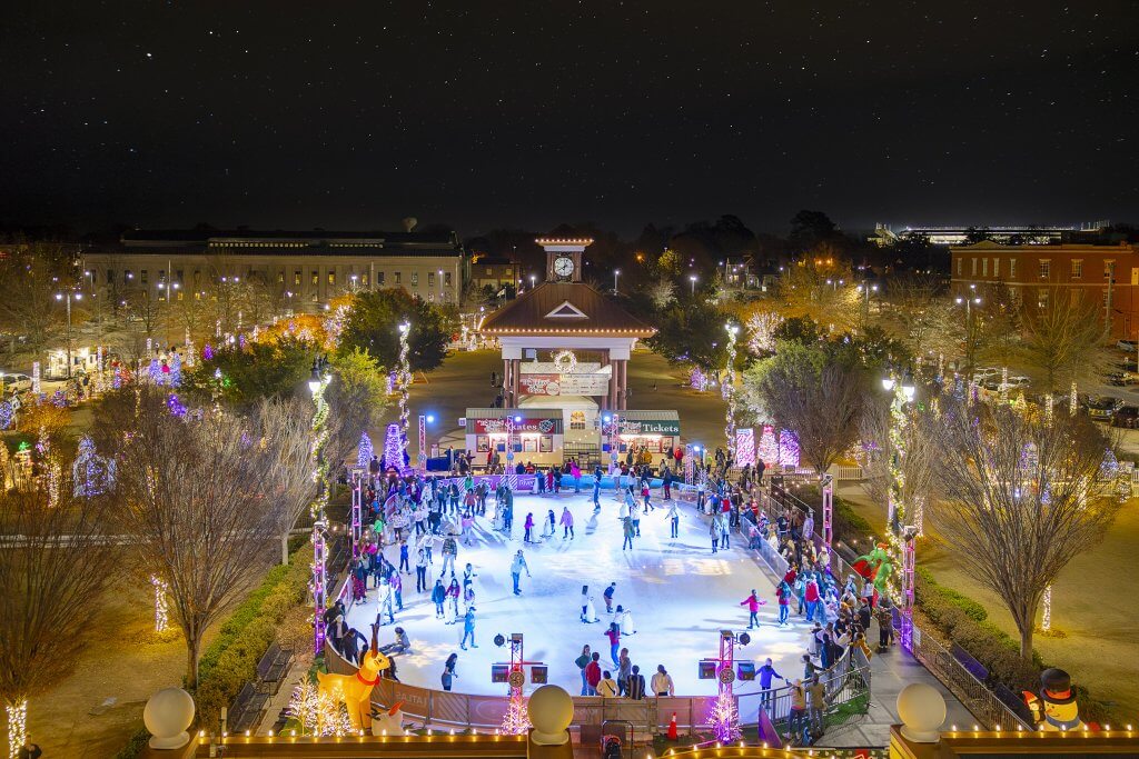 People ice skating at an outdoor rink decorated with festive holiday lights at night in Tuscaloosa, Alabama.