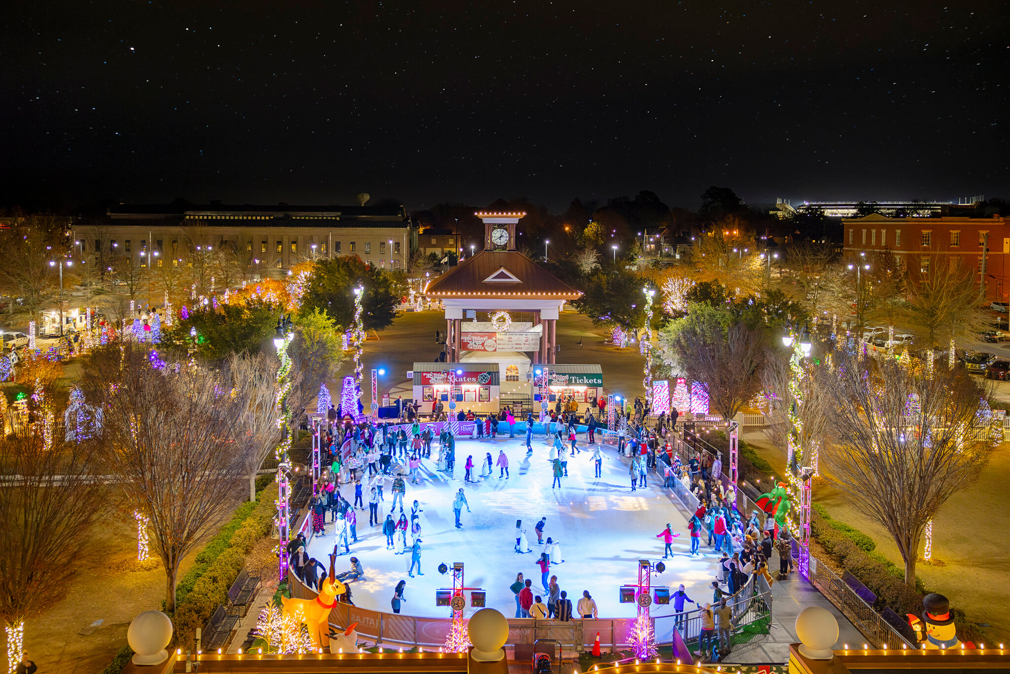 People ice skating at an outdoor rink decorated with festive holiday lights at night in Tuscaloosa, Alabama.
