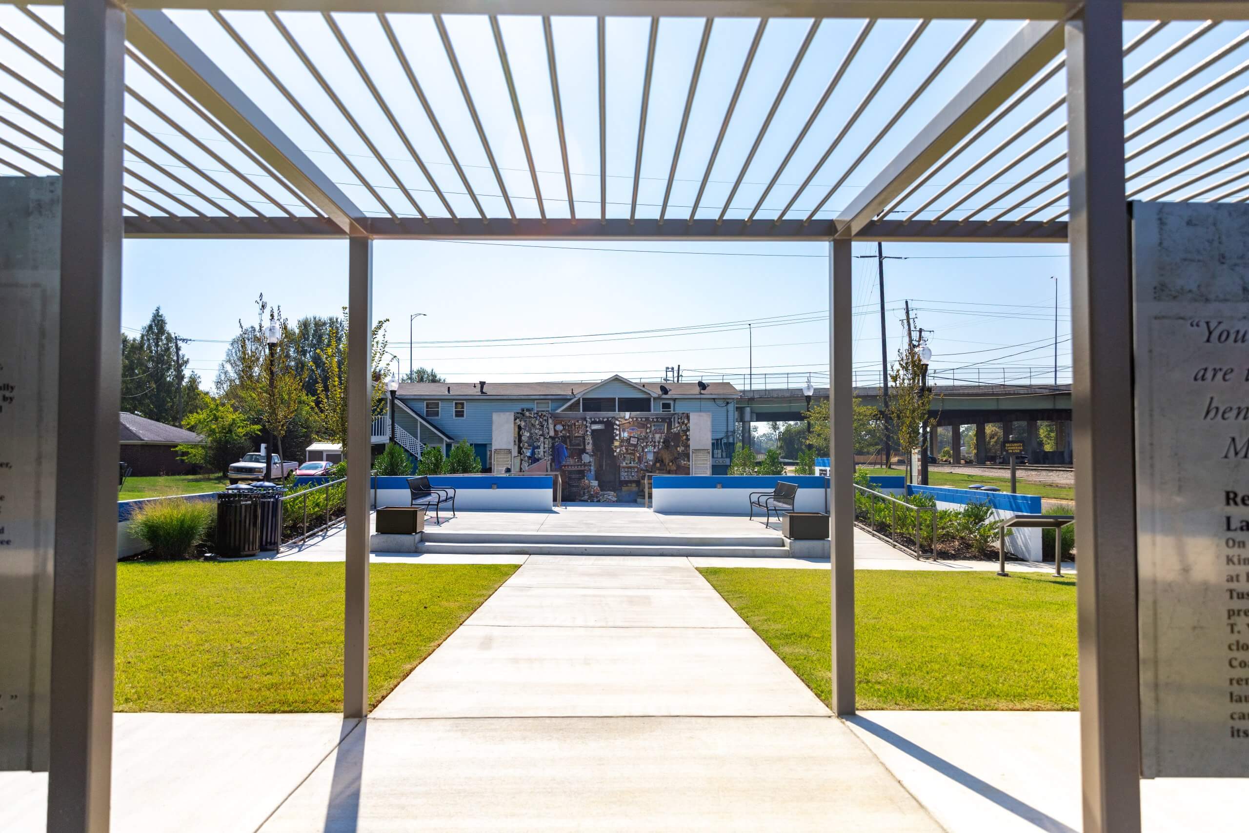 A concrete path leads through a pergola to a memorial site with benches in Tuscaloosa, Alabama.