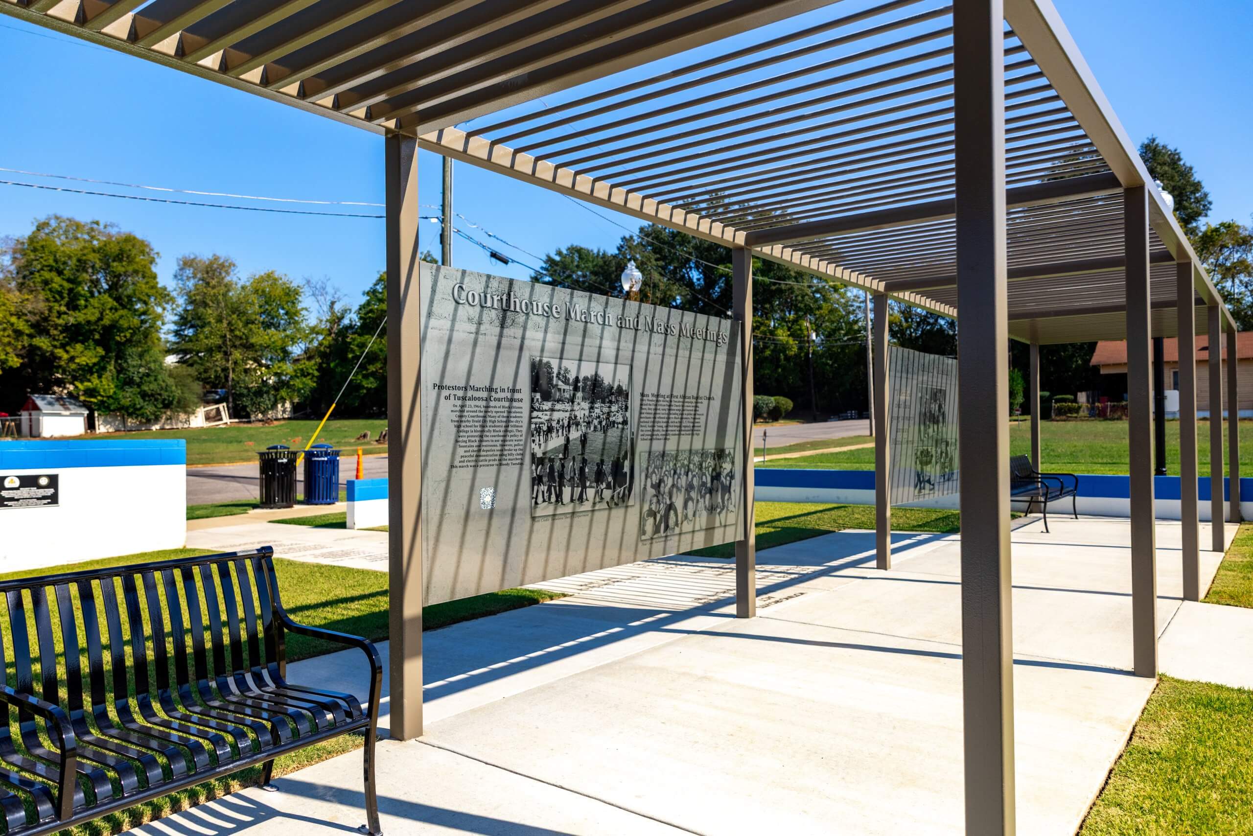 An outdoor historical marker with informational panels under a modern metal pergola in Tuscaloosa, Alabama.